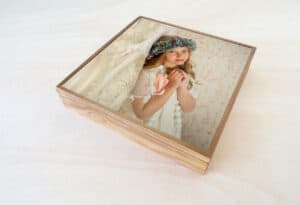 Niña con vestido y flor en la cabeza viendo su reflejo en espejo de madera, recuerdo de momentos especiales en álbumes personalizados.