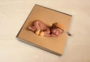 Dulce bebé durmiendo en un álbum de fotos con decoración de patitos y gorro tejido.